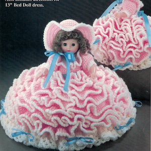May include: Two crocheted pillow dolls with ruffled pink and white skirts. The dolls are wearing blue ribbons and hats. The text on the image reads "10 1/2" Pillow Doll..... Half doll body attaches to a crocheted pillow base to create a firmly stuffed skirt. Also includes directions for 13" Bed Doll dress."