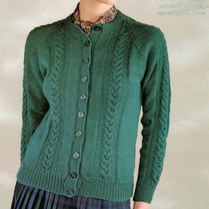 May include: A green knitted cardigan with a cable knit pattern and button fastening. The cardigan has a round neckline and long sleeves.