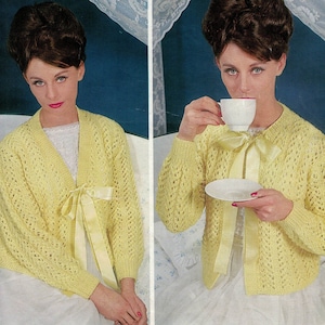 May include: A yellow knitted cardigan with a lace pattern and a satin ribbon tie. The cardigan is worn by a woman with a bouffant hairstyle.