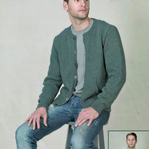 Puede incluir: Un cárdigan verde con botones, cuello redondo y dos bolsillos delanteros. El cárdigan se lleva sobre una camiseta gris de cuello redondo y se combina con vaqueros azules. El modelo está sentado en un taburete gris.