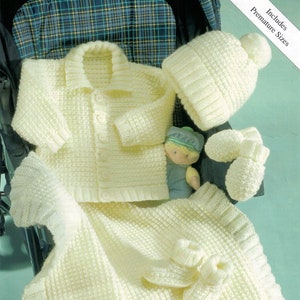 May include: A set of knitted baby clothes in a cream color, including a cardigan, hat, booties, and mittens. The set is laid out on a stroller.