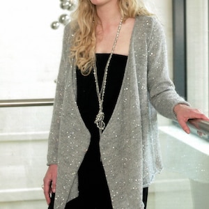May include: A light grey cardigan with scattered sequins. The open-front sweater has long sleeves and a draped design. The cardigan is paired with a black top and trousers, and a long silver necklace.