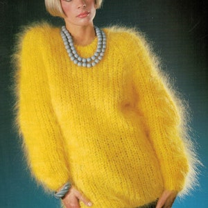 May include: A yellow fuzzy sweater with a round neckline and long sleeves. The sweater has a fluffy texture and is worn by a person with short blonde hair. The person is wearing a gray beaded necklace.