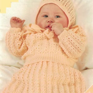 May include: A baby wearing a peach-colored knitted outfit, including a bonnet, long-sleeved top, and skirt. The outfit is made of a delicate, open-weave knit. The text on the image reads "16-22 inch" and "4 sizes".