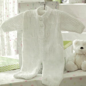 May include: White knitted baby onesie with a button fastening. The onesie is hanging on a hanger and has a ribbed texture.