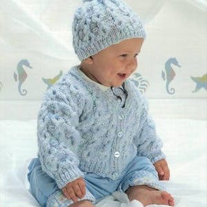 May include: A light blue knitted baby cardigan with a button closure and matching hat. The cardigan and hat feature a textured cable knit pattern.