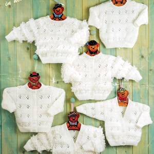 Könnte beinhalten: Mehrere weiße Strickpullover und -jacken werden auf Holzbügeln mit Teddybärköpfen präsentiert. Die Pullover haben verschiedene Texturen und Knopfverschlüsse. Der Text "Knitted with love in new soft blend Peter Pan" ist sichtbar.