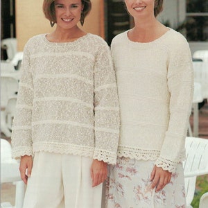 May include: Two women wearing white sweaters with crocheted trim. The woman on the left is wearing white pants, and the woman on the right is wearing a floral skirt.