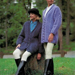May include: Two women wearing knitted coats and riding boots. One coat is a deep blue, buttoned down the front, and the other is a lighter purple. Both are paired with white riding pants and black boots. The background is a green, grassy area.