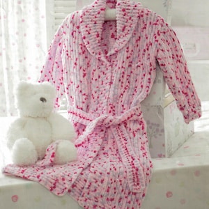 Pode incluir: Um roupão de malha rosa e roxo com gola de xale e cinto de laço. O roupão é feito de um fio macio e felpudo e tem um padrão salpicado.