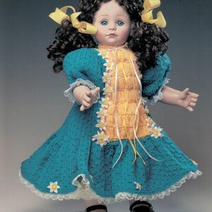 May include: A porcelain doll with blue eyes and dark curly hair adorned with yellow bows. The doll wears a teal and yellow knitted dress with white lace trim and flower accents. Black shoes complete the outfit.