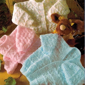 Op de afbeelding: Drie gebreide baby-vestjes in roze, blauw en wit met een knoopsluiting. De vestjes zijn gemaakt met een textuur-steek en hebben een zachte, knusse uitstraling.