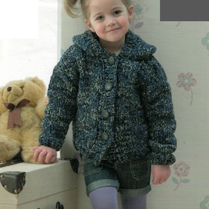 May include: A child wearing a blue and gray knit cardigan with large buttons. The cardigan is paired with denim shorts and purple tights. A teddy bear and a white trunk are in the background.