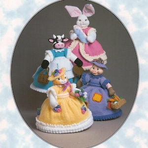 May include: Four knitted dolls dressed in colorful dresses. A cow doll in a blue and white dress, a bunny doll in a pink dress, a pig doll in a purple dress, and a cat doll in a yellow dress.