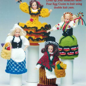 May include: Four knitted doll egg cosies, each dressed in a different traditional costume. The dolls are wearing a Spanish, German, Welsh, and Dutch costume. The text "Liven up your breakfast table! Four Egg Cosies to knit using double knit yarn." is printed above the dolls.