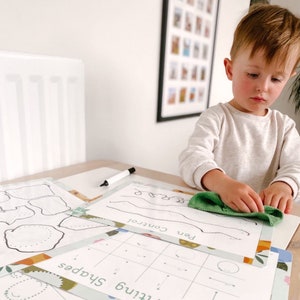 May include: A child is working on a set of printable worksheets with a green wipe. The worksheets include activities for learning shapes, pen control, and fine motor skills. The worksheets are printed on white paper with a green and orange border.