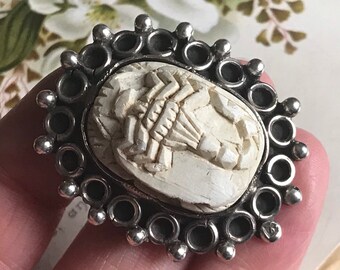 May include: A silver ring with a white carved scarab beetle design. The ring is surrounded by a decorative border of silver circles and beads.