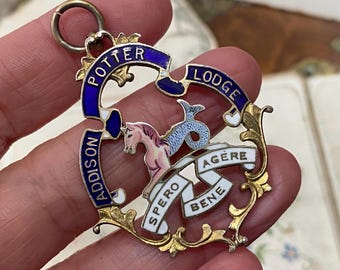 May include: A vintage pendant with the words "POTTER LODGE" and "ADDISON" in blue enamel. The pendant features a seahorse and a banner with the words "SPERO BENE" and "AGERE". The pendant has gold-coloured filigree accents.