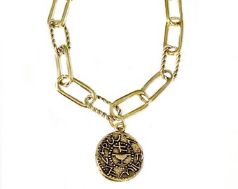 Puede incluir: Un brazalete de cadena dorada con un colgante redondo que presenta texto hebreo y un diseño de cáliz.