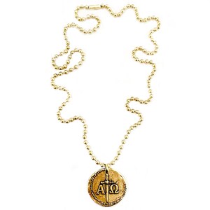 May include: A gold necklace with a round pendant featuring a sword and the letters Alpha and Omega. The necklace is made of a ball chain.