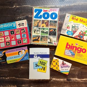 May include: A collection of vintage board and card games including Memory, Zoo Lotto, Old Maid, a four-pack of children's card games, Numbers Flashcards, a yellow Bingo box, and a small box labeled Crafty Butterfly Magic Square with butterfly graphics.