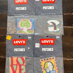 May include: Four Levi's patches in original packaging. The patches feature various designs, including a tree, a rainbow, the word "LOVE", and a postage stamp with a person giving a peace sign and the word "FREE".