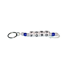 May include: A keychain with the word "FORD" spelled out in white letter beads. The beads are strung together with blue and white beads, and attached to a silver keyring.