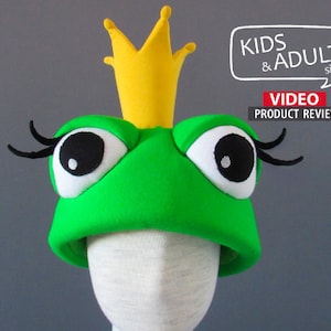 May include: Green frog hat with a yellow crown and black eyelashes. The hat is made of soft fabric and has a white face with black eyes. The hat is available in kids and adult sizes.  VIDEO PRODUCT REVIEW