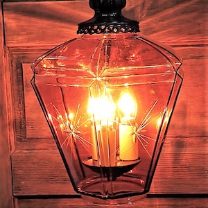 May include: A vintage amber glass pendant light fixture with a black metal frame and star-shaped etched details. The light is on and illuminates the room with a warm glow.