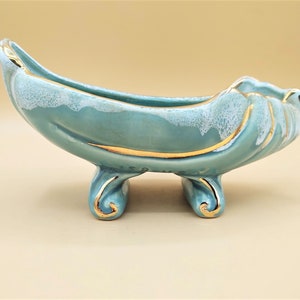 Può includere: Un vaso da fiori in ceramica turchese con dettagli dorati e tre gambe. Il vaso ha una smaltatura bianca con un motivo maculato.