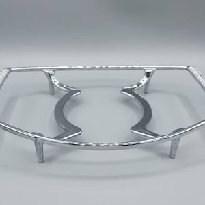 May include: A silver metal rack with two curved supports and four legs. The rack is designed to hold a dish or other object above a heat source.