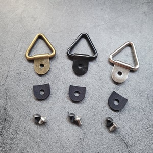 May include: Three triangle-shaped metal picture hangers in gold, black, and silver with a screw hole in the bottom. Each hanger comes with a black rubber washer and a silver screw.