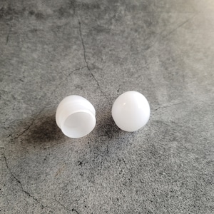 May include: Two white plastic light bulb covers, one is whole and the other is open, showing the inside.