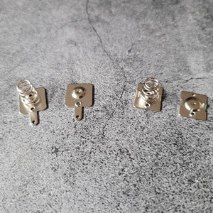 May include: Four silver battery contacts with spring loaded terminals. The contacts are square shaped with rounded corners and have a small hole in the center.