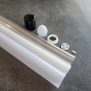 Puede incluir: Un tubo de luz blanco y transparente con una tapa de extremo negro, una tapa de extremo blanco, un difusor blanco, una placa de circuito blanco y una pequeña pieza plateada.