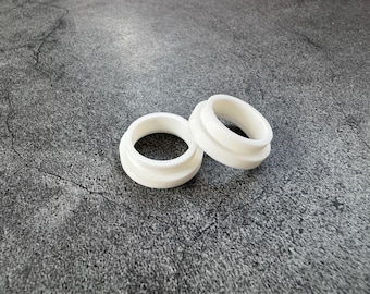 May include: Two white, circular, stepped rings with a smooth, matte finish. Each ring features a wider base section and a narrower top section, creating a distinct tiered profile. The objects are solid in color and have a uniform, clean appearance.