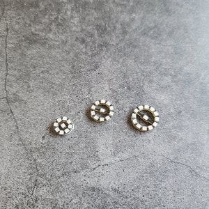 May include: Three silver-toned round buttons with white rhinestones arranged in a circle around the edge. The buttons are different sizes.
