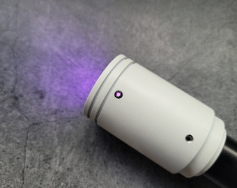 May include: A white cylindrical device with a purple light emanating from it. The device has a small black button on the side.