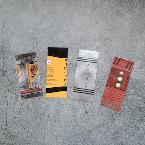 Peut inclure: Quatre cartes rectangulaires avec des motifs différents. La première carte est jaune avec du texte noir et un symbole rouge. La deuxième carte est grise avec du texte noir. La troisième carte est rouge avec des cercles blancs et verts. La quatrième carte est marron avec une image noir et blanc d'un robot.
