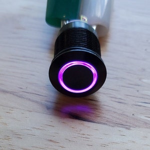 May include: A black push button switch with a purple LED ring around the button.