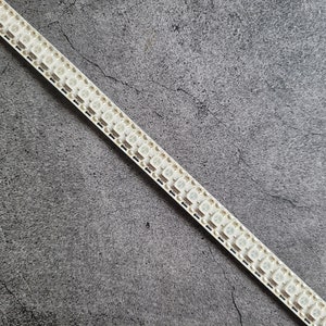 May include: A white LED strip light with a row of small, square lights. The strip is on a gray, textured surface.