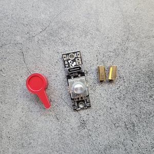 May include: A small black circuit board with a silver knob and two gold-coloured connectors. A red plastic toggle switch is also pictured.