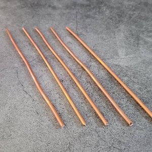 May include: Five copper wire pieces, each with a rounded end, are arranged on a gray surface.