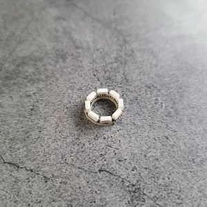 May include: A silver ring with a circle of white rectangular stones.