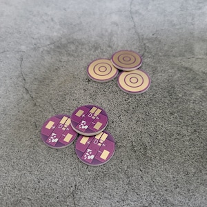 May include: Five small, round, gold-colored electronic components with a concentric circle design. Four smaller, round, purple electronic components with a white plus and minus sign and the letter D printed on them.