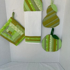 May include: Set of four green quilted kitchen accessories, including a potholder, a dish towel, a pear-shaped pot holder, and a round apple-shaped pot holder.