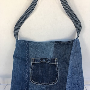 May include: A blue denim tote bag with a gingham strap and a front pocket with a bow. The bag is made from recycled denim.