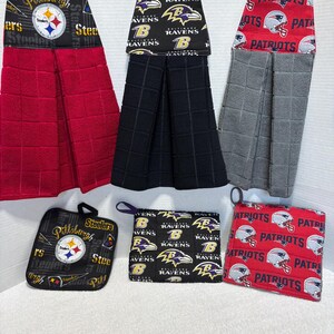May include: A collection of kitchen textiles featuring NFL team logos. Includes red and black hanging towels, pot holders, and oven mitts. The logos include the Pittsburgh Steelers, Baltimore Ravens, and New England Patriots.