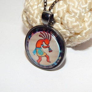Könnte beinhalten: Eine silberne Kettenkette mit einem runden Anhänger, der eine farbenfrohe Illustration eines indianischen Tänzers zeigt. Der Anhänger hat einen schwarzen Rand und einen weißen Hintergrund.