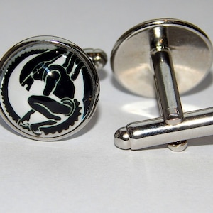 May include: A pair of silver cufflinks with a black and white image of an alien creature on one cufflink.